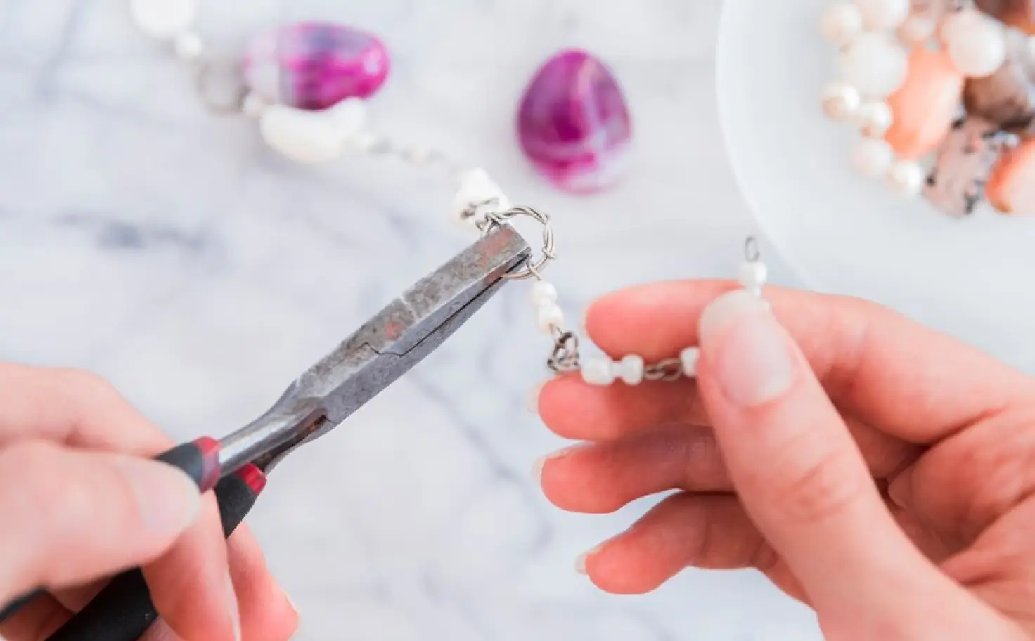 Pliers closing the fitting on a pink gemstone earring