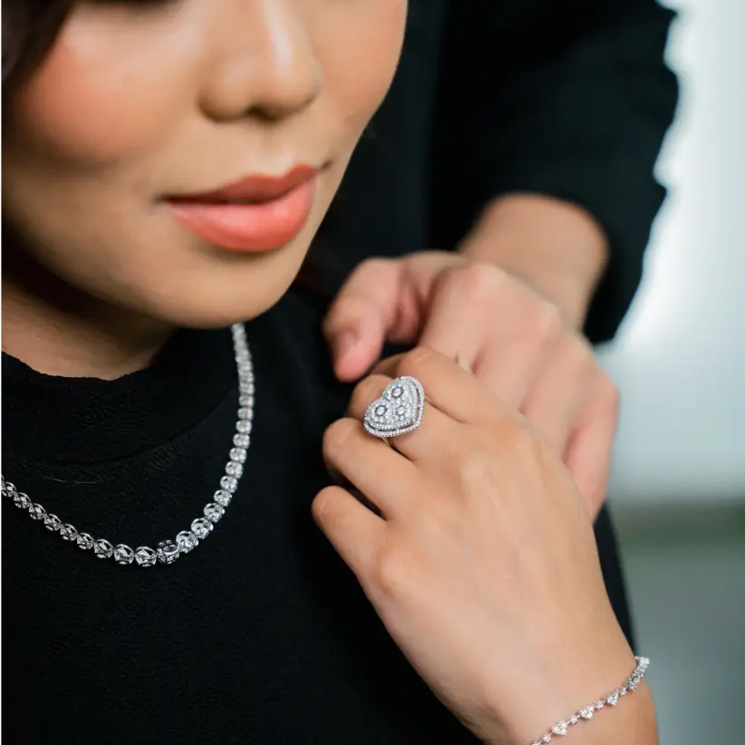 A diamond cocktail ring worn against a black knit, with a tennis necklace above