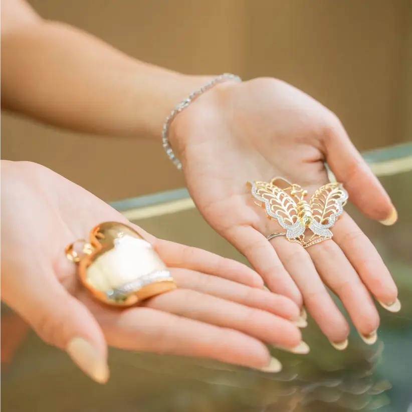 Two open palms holding a gold butterfly brooch and a pearl piece